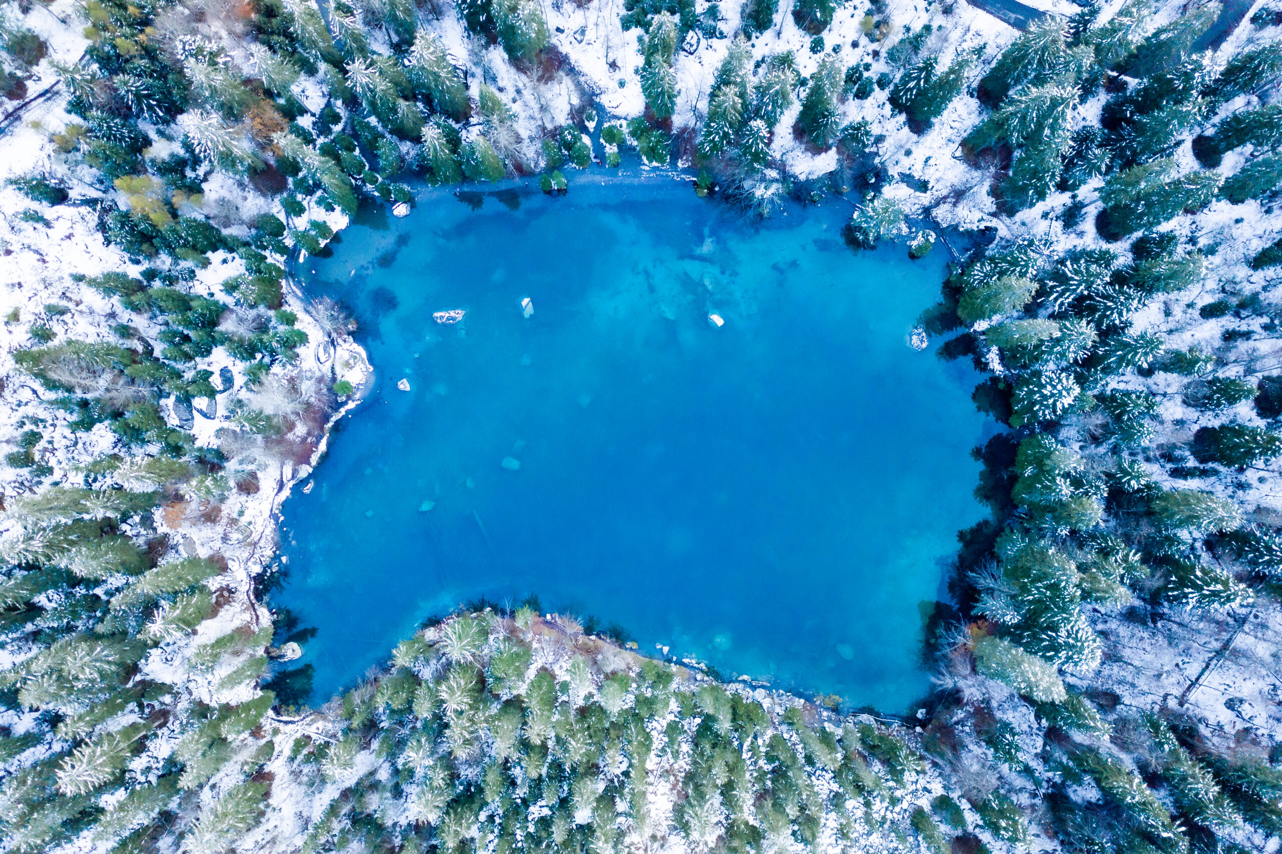 Aerial photograph of Lac Vert in the French Alps, it's winter and the water is frozen and there is snow on the trees around the water.